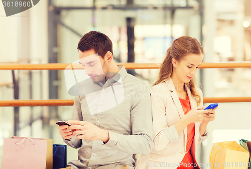 Image of couple with smartphones and shopping bags in mall