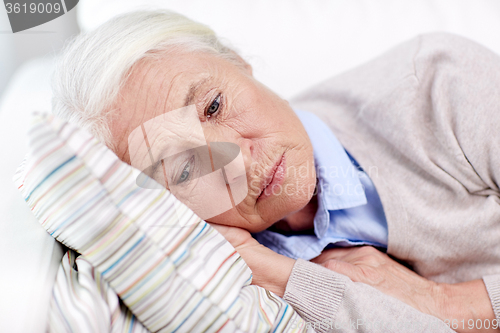 Image of sad senior woman lying on pillow at home