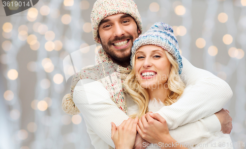 Image of happy couple in winter clothes hugging over lights