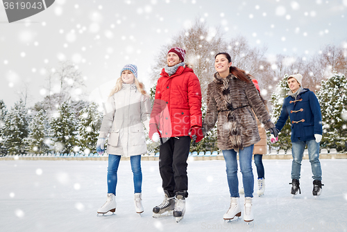 Image of happy friends ice skating on rink outdoors