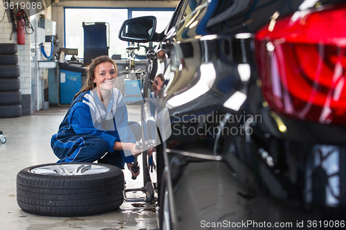 Image of Female service mechanic changing the front tire of a car