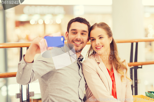 Image of happy couple with smartphone taking selfie in mall