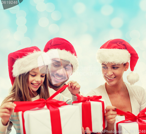 Image of happy family in santa hats sitting with gift boxes