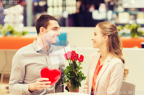 Image of happy couple with present and flowers in mall