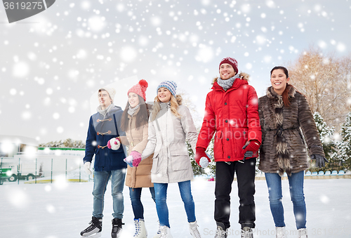 Image of happy friends ice skating on rink outdoors