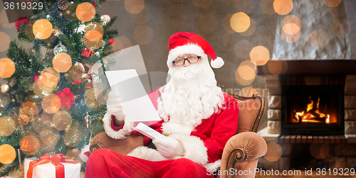 Image of santa claus reading letter in armchair at home