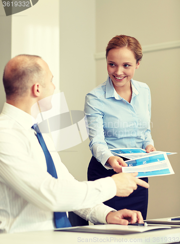 Image of smiling woman giving papers to man in office