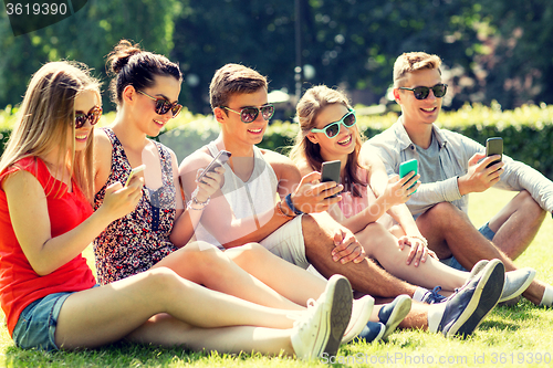 Image of smiling friends with smartphones sitting on grass