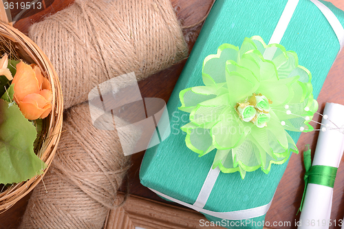 Image of green christmas gift box, white paper with bow on wooden table.