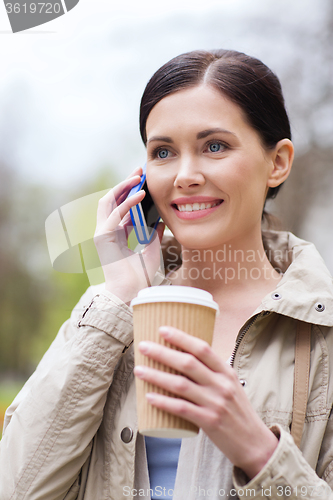 Image of smiling woman with smartphone and coffee in park