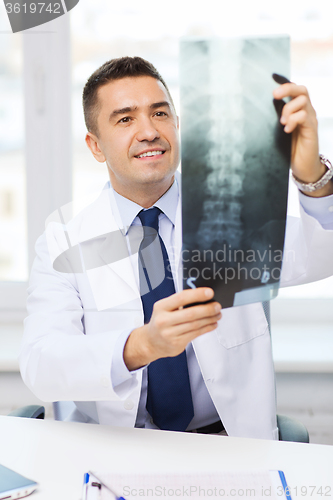 Image of smiling male doctor in white coat looking at x-ray