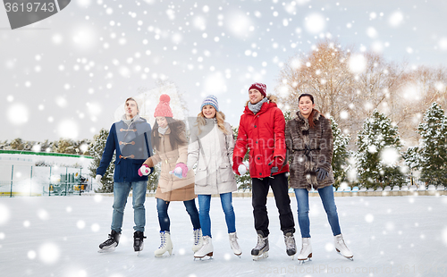 Image of happy friends ice skating on rink outdoors