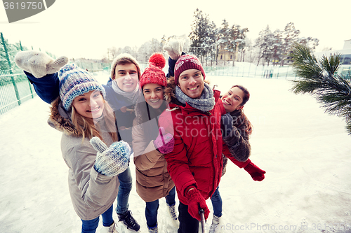 Image of happy friends with smartphone on ice skating rink