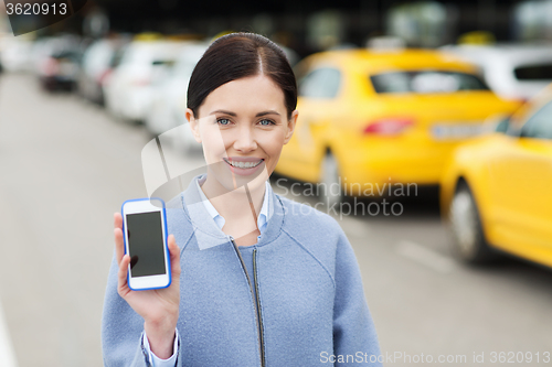 Image of smiling woman showing smartphone over taxi in city