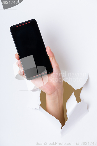 Image of Hand holding mobile phone bursting through paper