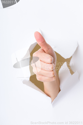 Image of Thumb up hand gesture break through the paper wall