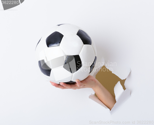 Image of Soccer ball hold with woman hand break through the paper wall