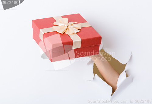 Image of Hand hold with present box break through the paper wall