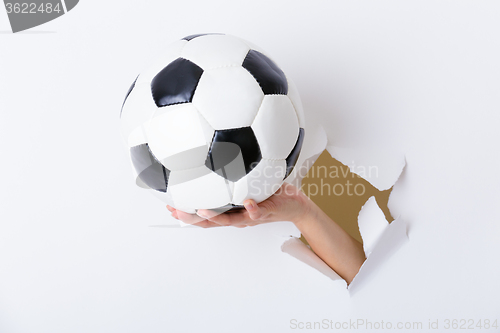 Image of Hand holding soccer ball through the paper hole 