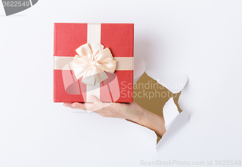 Image of Woman hand hold with present box break through the paper wall