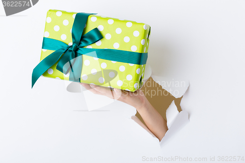 Image of Hand break through paper with green present box