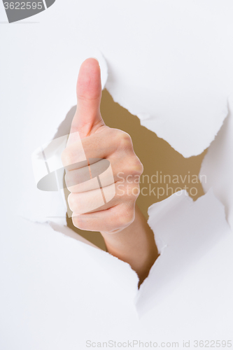 Image of Thumb up hand gesture through a hole in paper