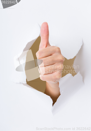 Image of Hand with thumb up through a hole in paper