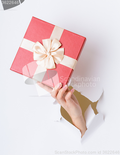 Image of Hand hold with giftbox break through the paper wall