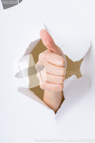 Image of Hand with thumb up through a hole in paper