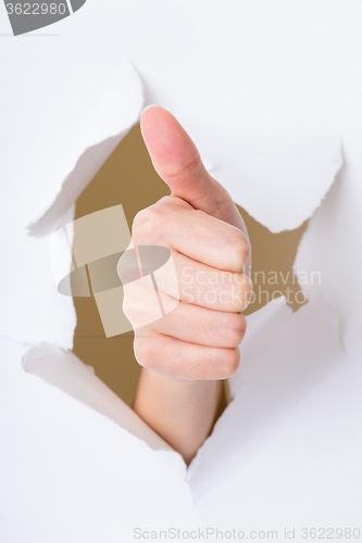 Image of Hand with thumb up through a hole in paper