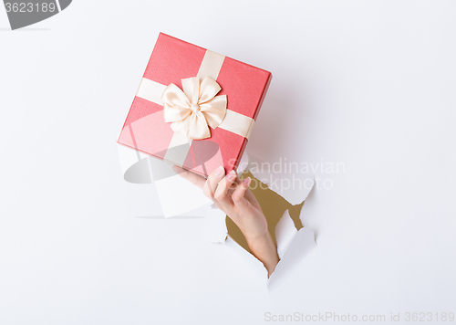 Image of Hand holding pink gift box through the paper hole 