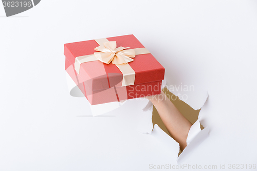 Image of Hand holding giftbox through the hole in paper