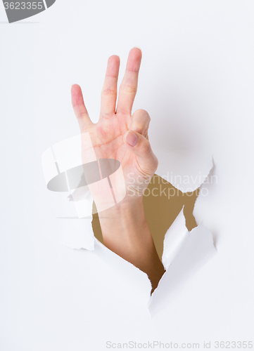 Image of Finger showing ok sign bursting through paper