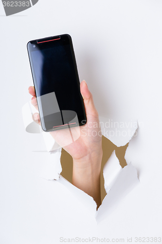 Image of Hand break through paper and hold with blank screen of cellphone