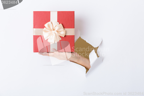 Image of Hand break through paper with red present box