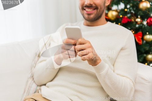 Image of smiling man with smartphone at home for christmas