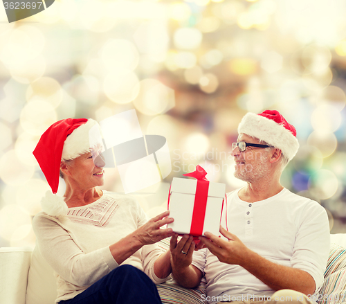 Image of happy senior couple in santa hats with gift box
