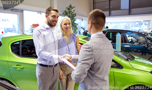 Image of happy couple with car dealer in auto show or salon