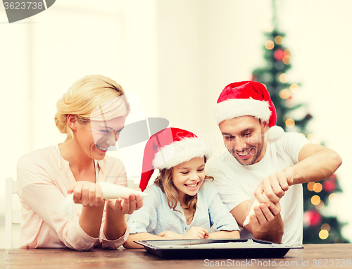 Image of happy family in santa helper hats making cookies