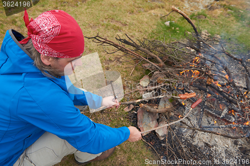 Image of hiking man prepare tasty sausages on campfire