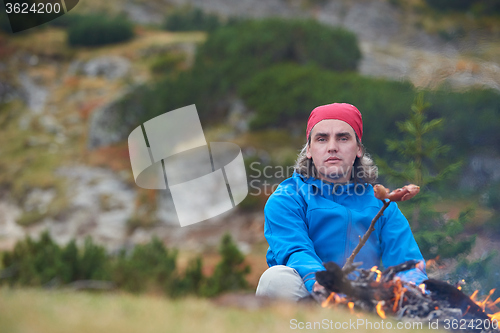 Image of hiking man prepare tasty sausages on campfire