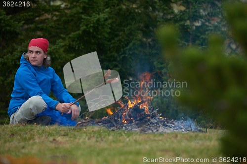 Image of hiking man prepare tasty sausages on campfire