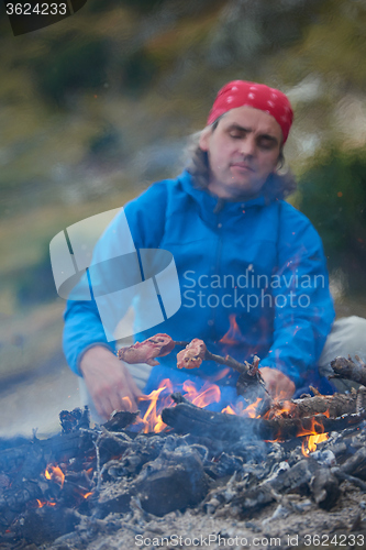 Image of hiking man prepare tasty sausages on campfire