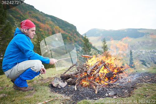 Image of hiking man prepare tasty sausages on campfire
