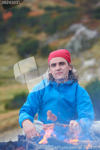 Image of hiking man prepare tasty sausages on campfire