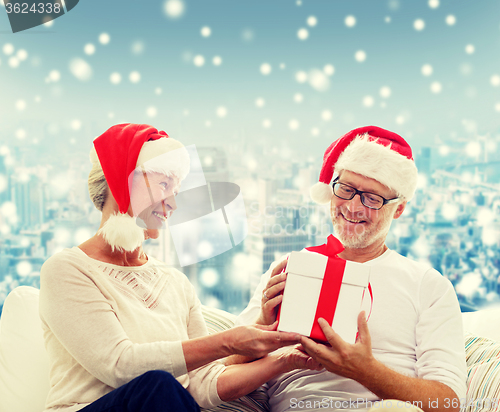 Image of happy senior couple in santa hats with gift box