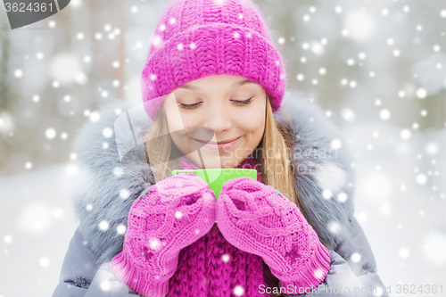 Image of smiling young woman with cup in winter forest