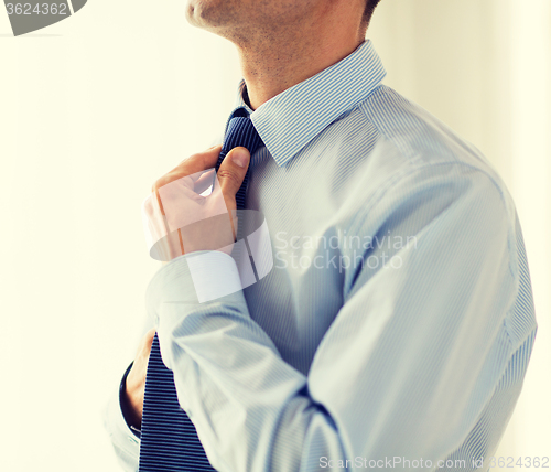 Image of close up of man in shirt adjusting tie on neck