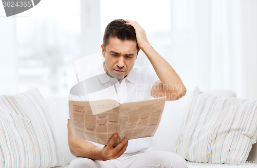 Image of sad man reading newspaper at home