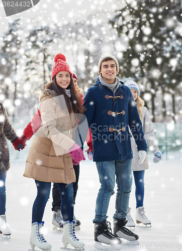 Image of happy friends ice skating on rink outdoors